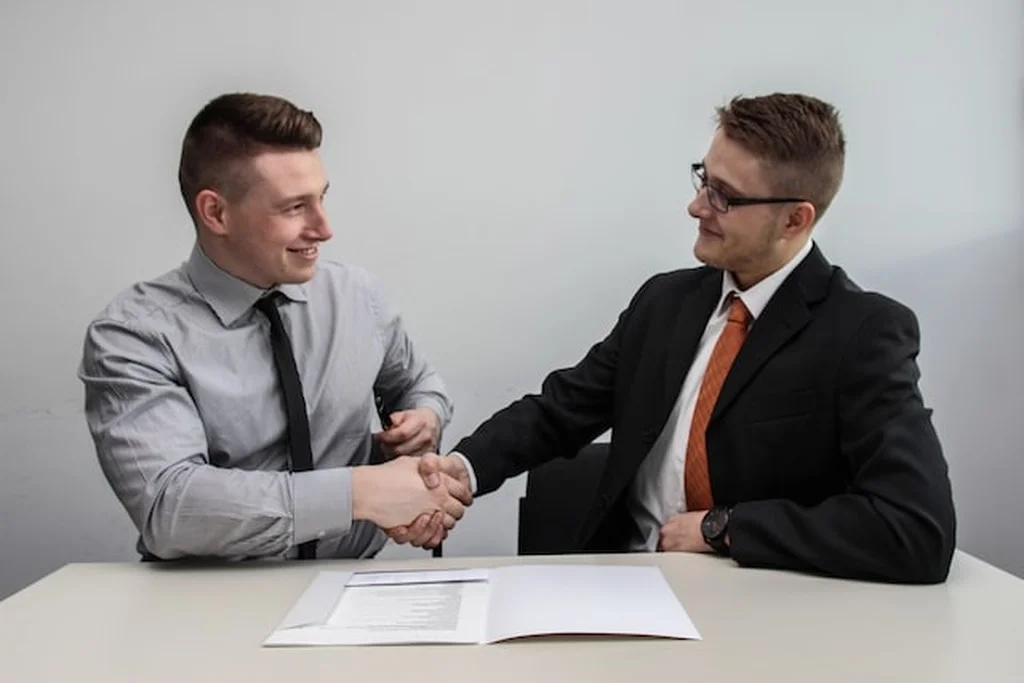 Dois homens de roupa social dando um aperto de mão e em frente deles há um contrato sobre a mesa, simbolizando um distrato imobiliário