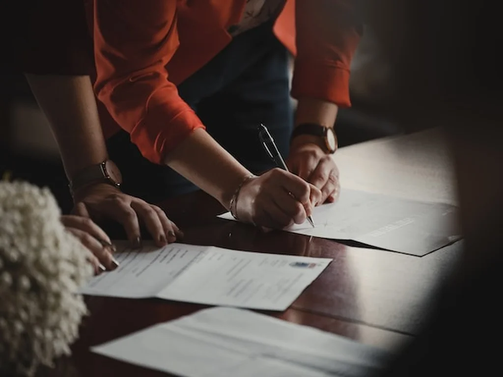 Pessoas firmando contratos que estão sobre a mesa, representando distrato imobiliário